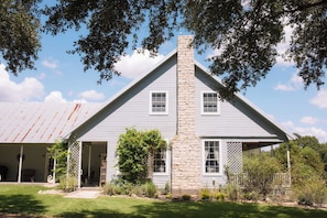A two-story house with a stone chimney, white siding, and a covered porch. - NEW | Wisteria Ranch | Perfect Round Top Escape (Round Top)