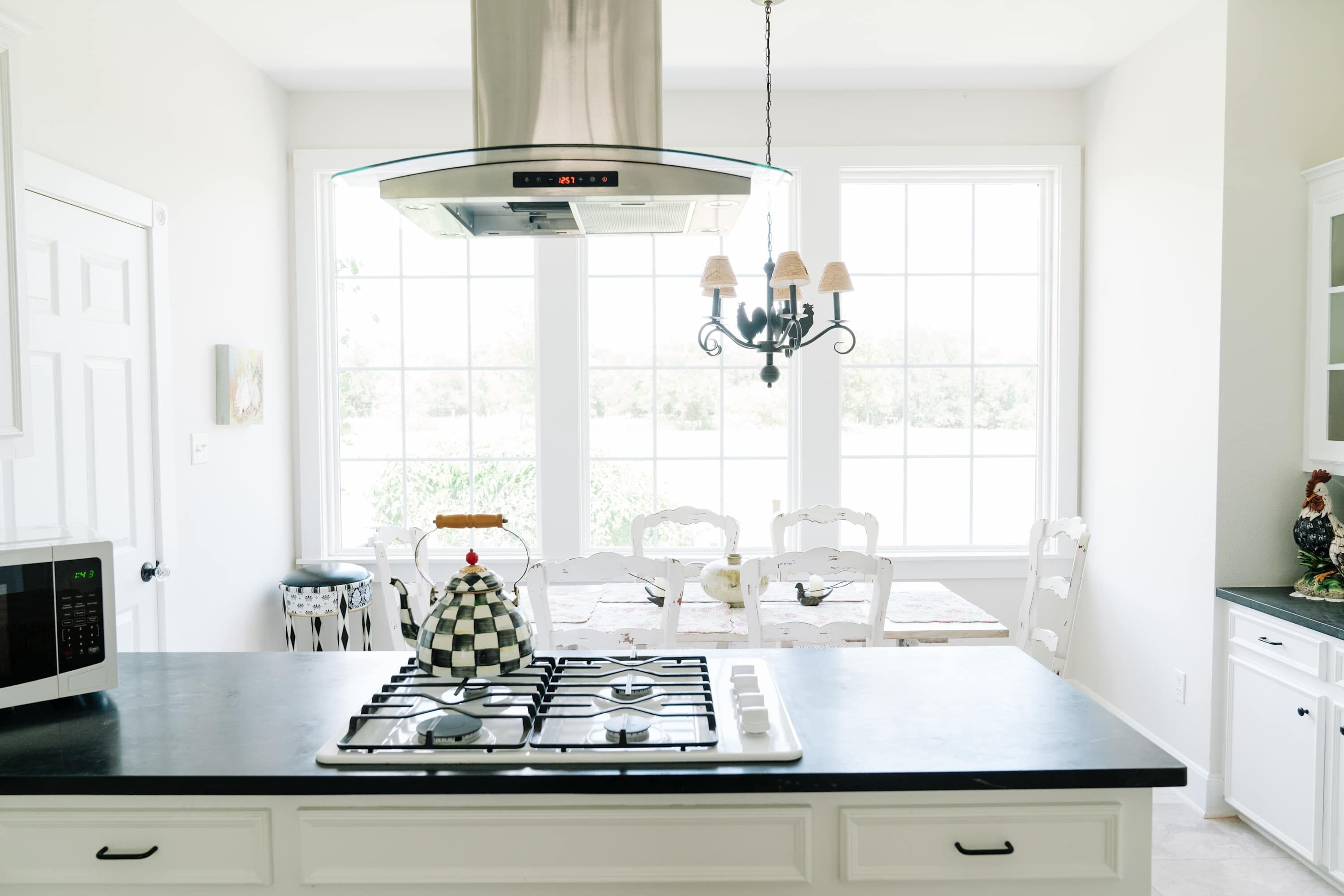 Una cocina con estufa a gas, microondas, candelabro y vistas al exterior a través de amplias ventanas.