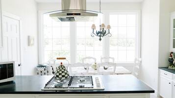 Una cocina con estufa a gas, microondas, candelabro y vistas al exterior a través de amplias ventanas.