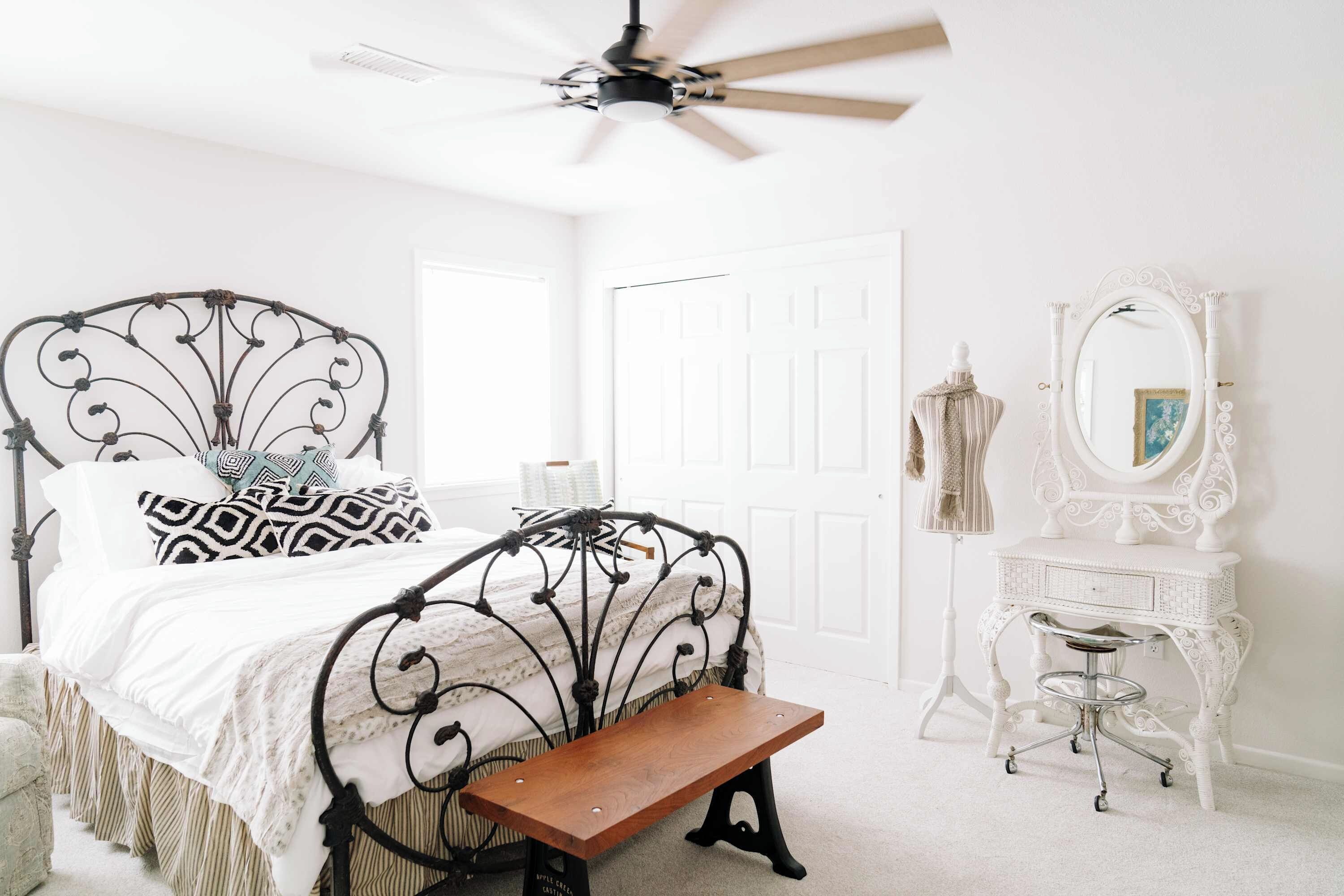 A bedroom with a bed, a bench, a dresser, a mirror, and a ceiling fan.