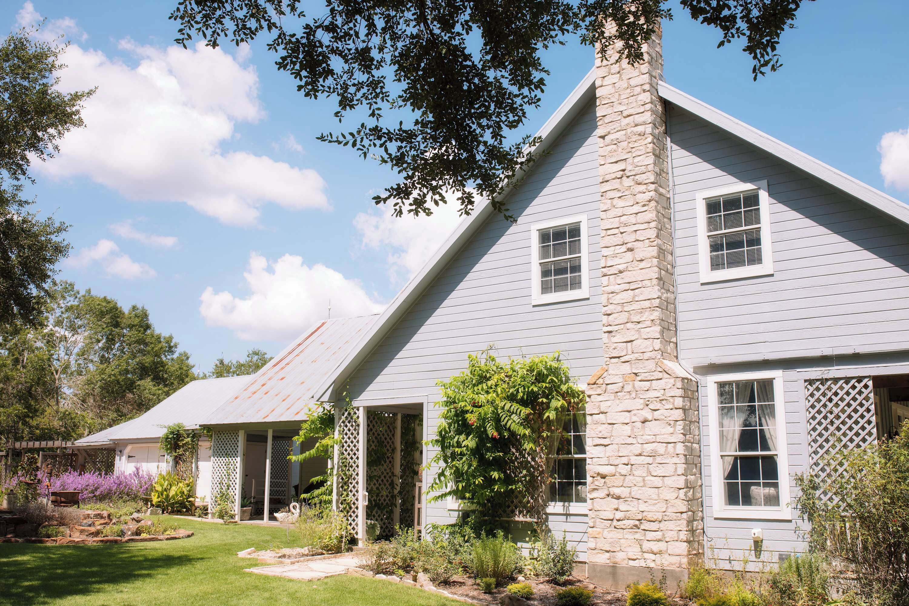 A two-story house with a stone chimney, a covered porch, and a well-maintained garden.