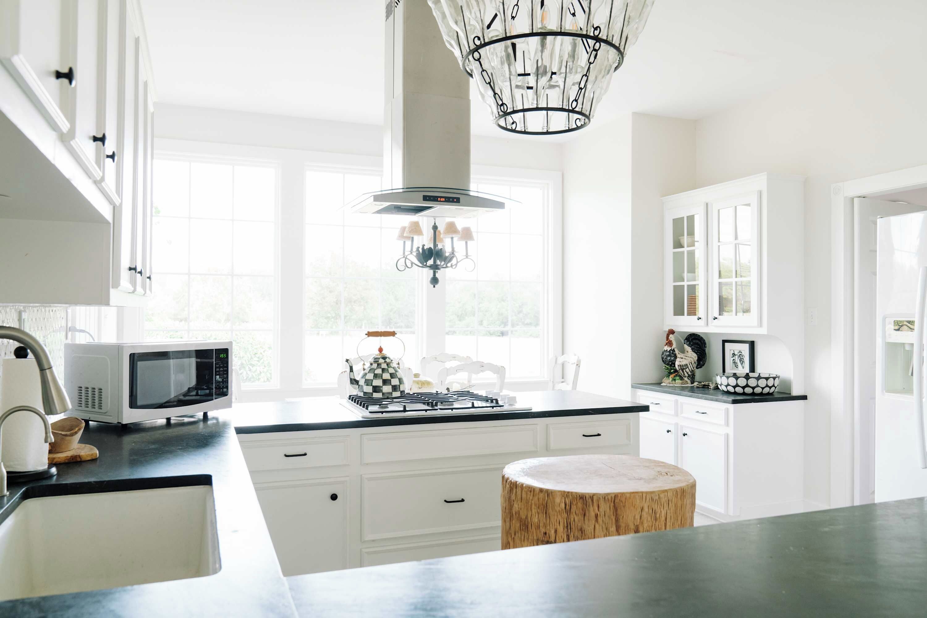 A bright kitchen with white cabinetry, a microwave, a gas stove, and a chandelier.