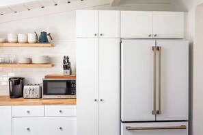 Eine Küche mit weißen Schränken, einem Edelstahl-Kühlschrank, einer Mikrowelle, einer Kaffeemaschine und einem Messerblock.