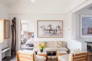 Ein modernes Wohnzimmer mit einer Couch, zwei Sesseln, einem Gemälde von Pferden und einer Holzskulptur.