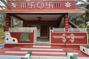 A building entrance with a red and white facade, a coconut-themed sign, and a gate with dollar sign decorations. - Coconut Sooru Homestay Channapatna (Kurnagere)