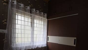 A bedroom with a bed, a ceiling fan, a window with curtains, and a wardrobe.