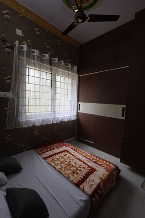 Ein Schlafzimmer mit einem Bett, einem Deckenventilator, einem Fenster mit Vorhängen und einem Kleiderschrank.