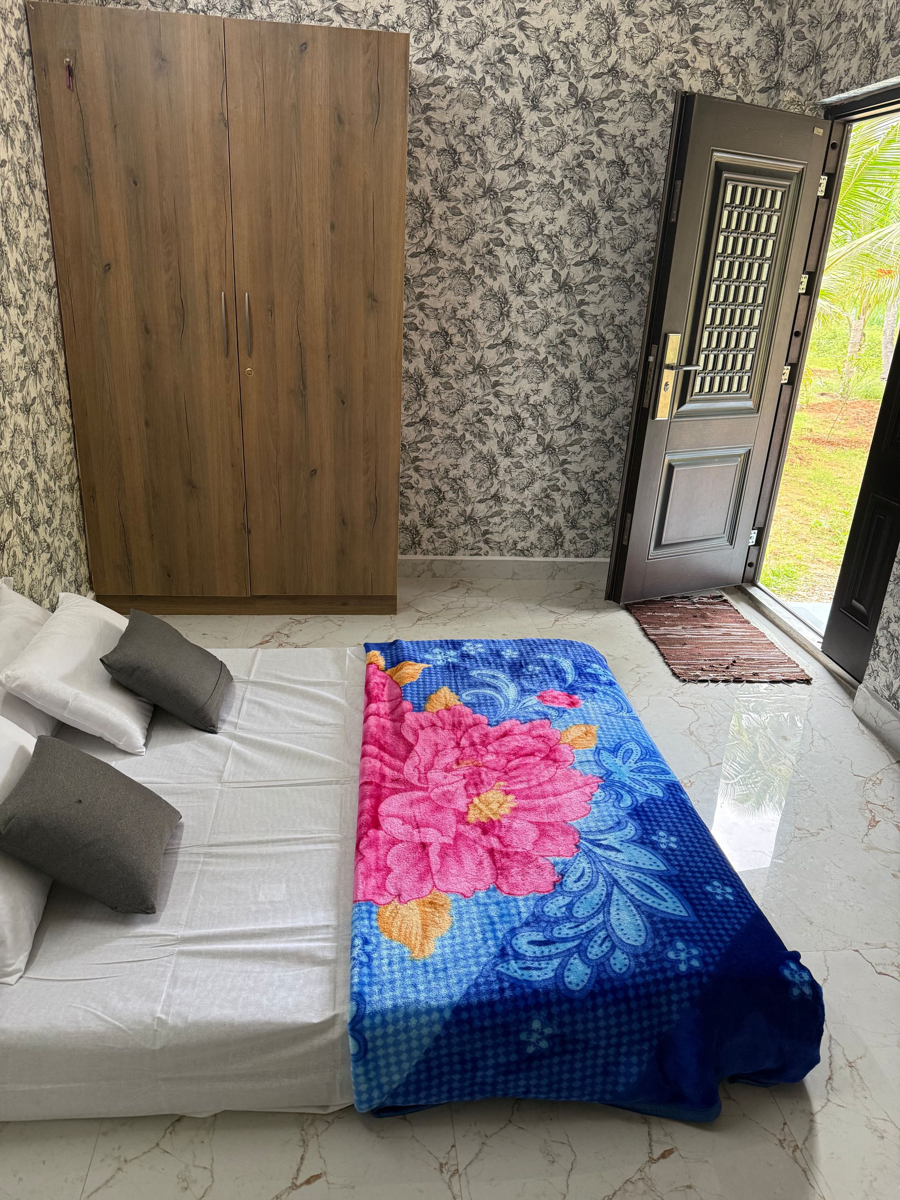 A room with a bed, a wooden wardrobe, a door with a metal grill, and a patterned wall.