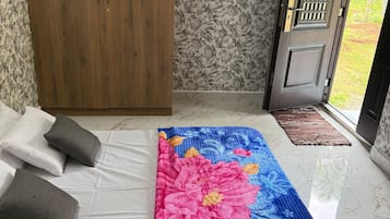 A room with a bed, a wooden wardrobe, a door with a metal grill, and a patterned wall.