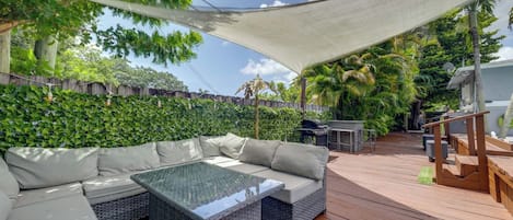Una terrazza esterna con zona salotto imbottita, un tavolo con piano in vetro e un pavimento in legno.