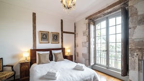 A bedroom with a large bed, two bedside lamps, a chandelier, and a view through a window.