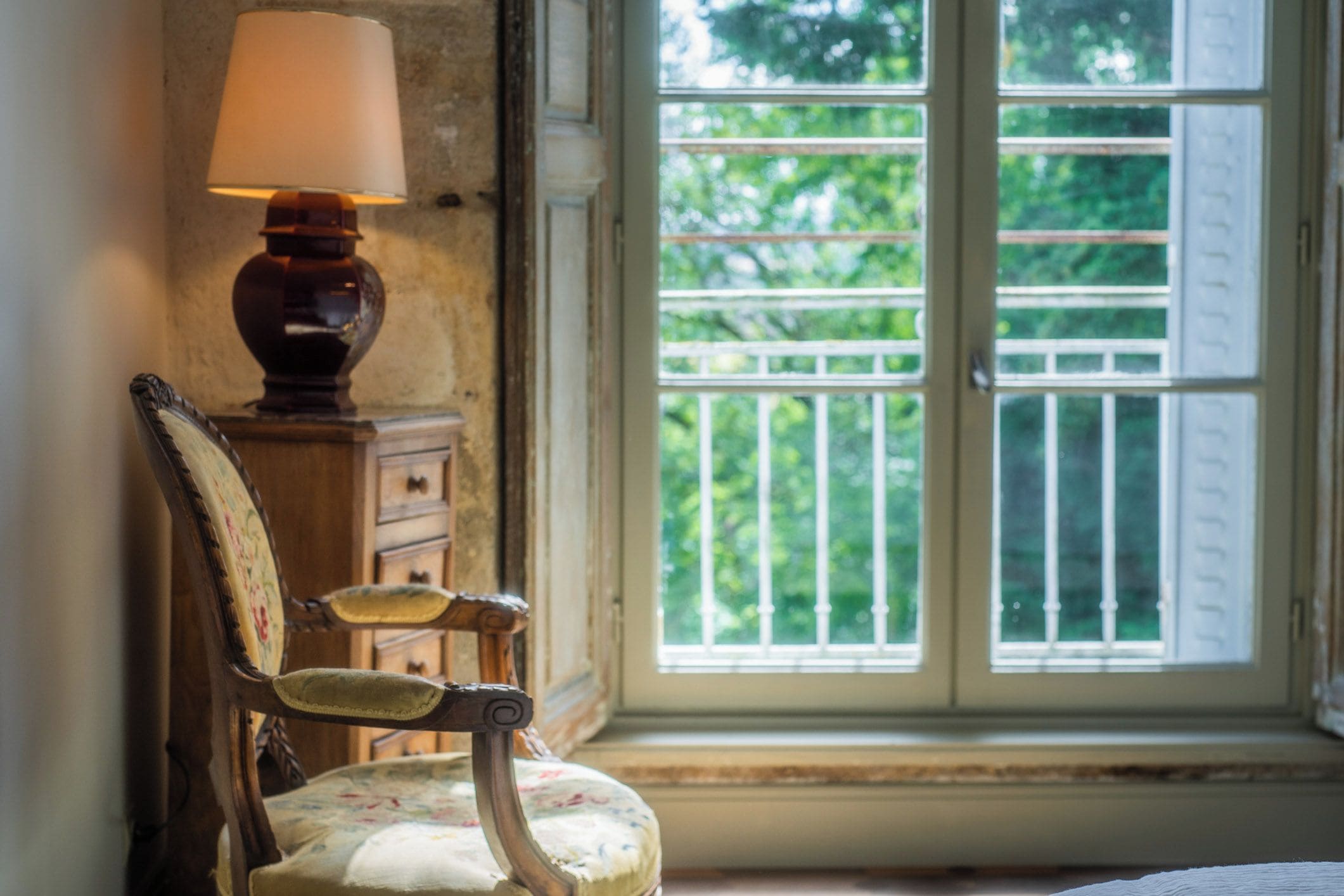 Une chaise à motifs floraux, une lampe et une fenêtre donnant sur un paysage verdoyant.