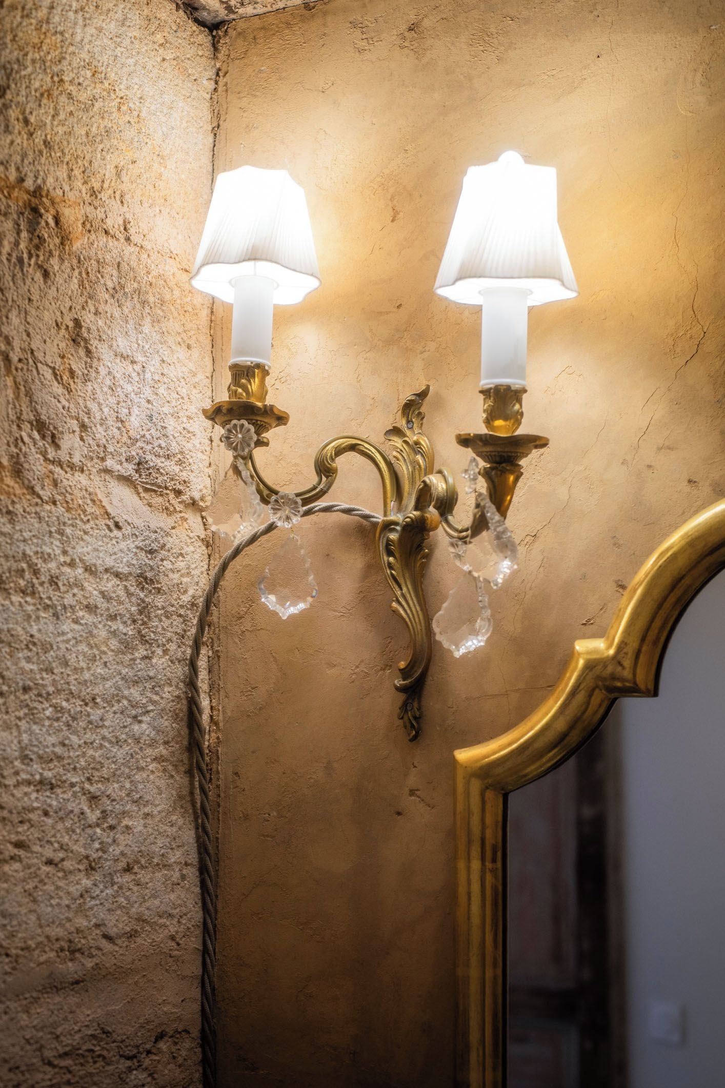 Een wandlamp met twee lampen, een structuurwand en een spiegel met gouden lijst.