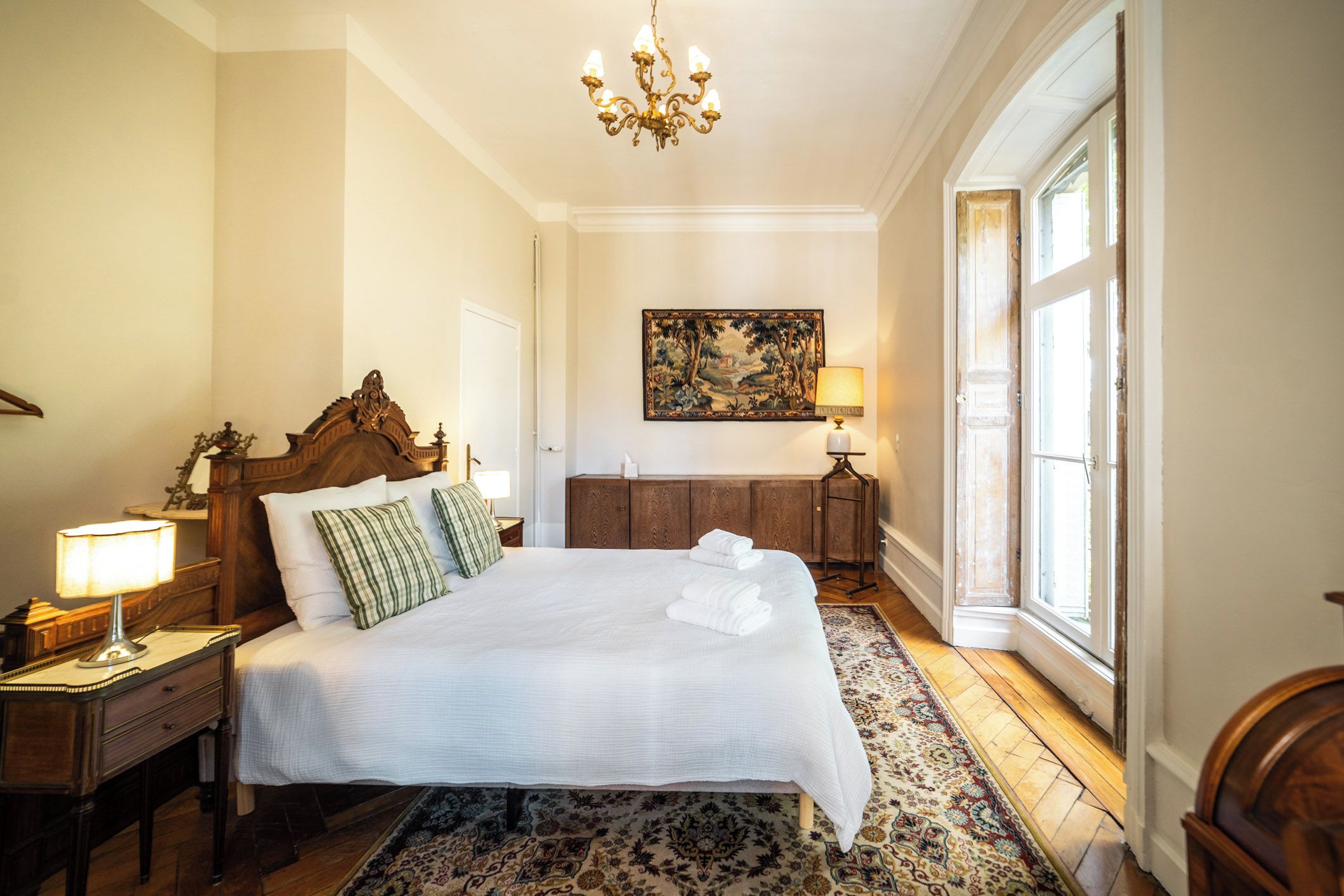 Habitación de hotel con una cama grande, un candelabro, un cuadro en la pared y vistas al exterior.