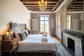 A bedroom with a large bed, a wooden headboard, a chandelier, a fireplace, and a large mirror. - Château de Sainte-Sévère (Sainte-Sévère-sur-Indre)