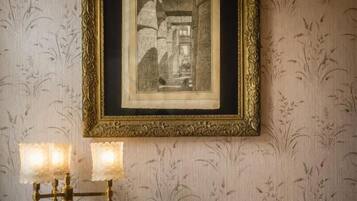 A framed black and white photograph on a wall with a patterned wallpaper background. Below the photo, there is a wall-mounted brass candelabra with three lit candles.