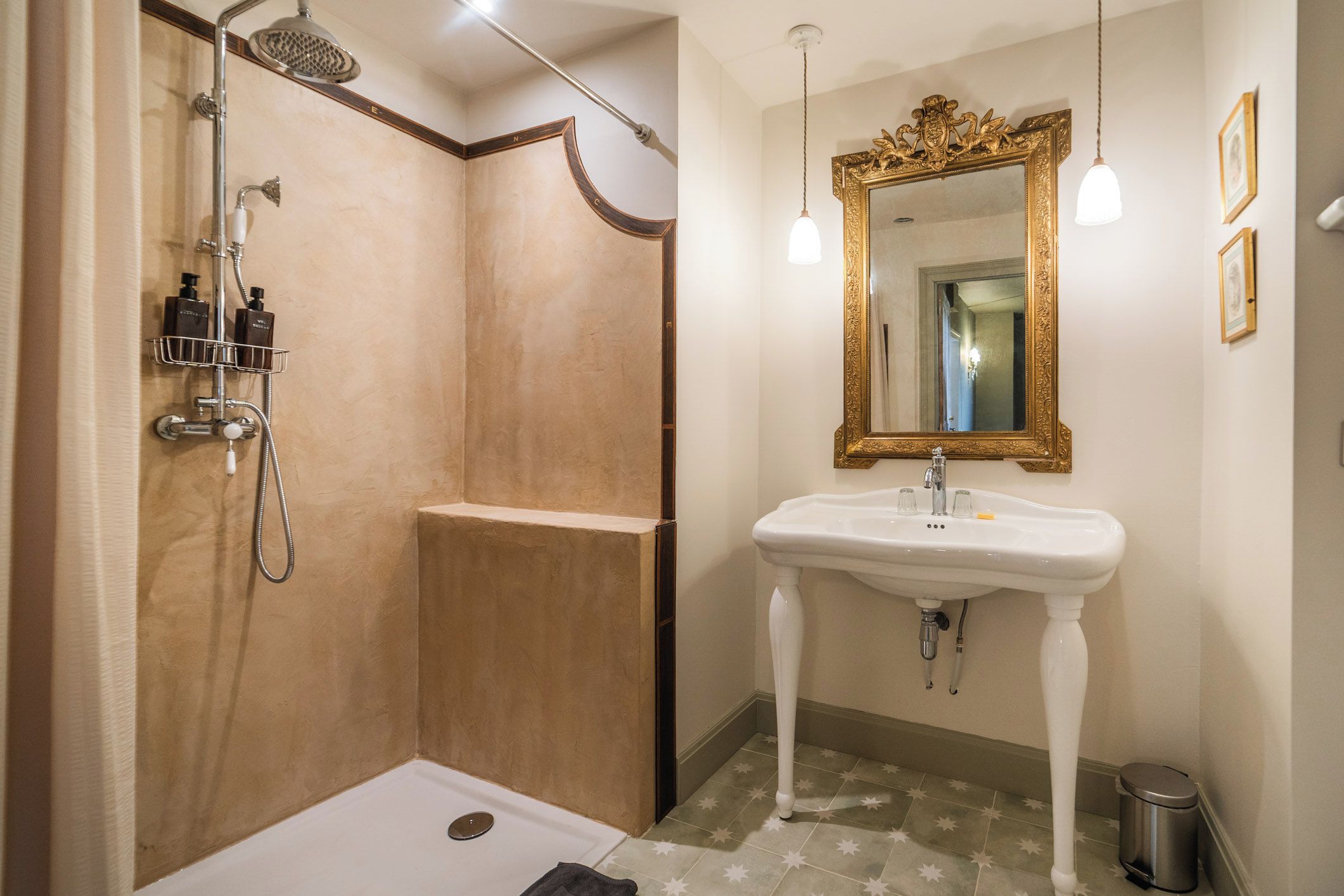 Une salle de bain dotée d’une douche à l’italienne, d’un lavabo sur colonne et d’un grand miroir encadré d’un cadre orné.