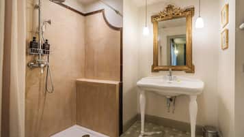 Une salle de bain dotée d’une douche à l’italienne, d’un lavabo sur colonne et d’un grand miroir encadré d’un cadre orné.