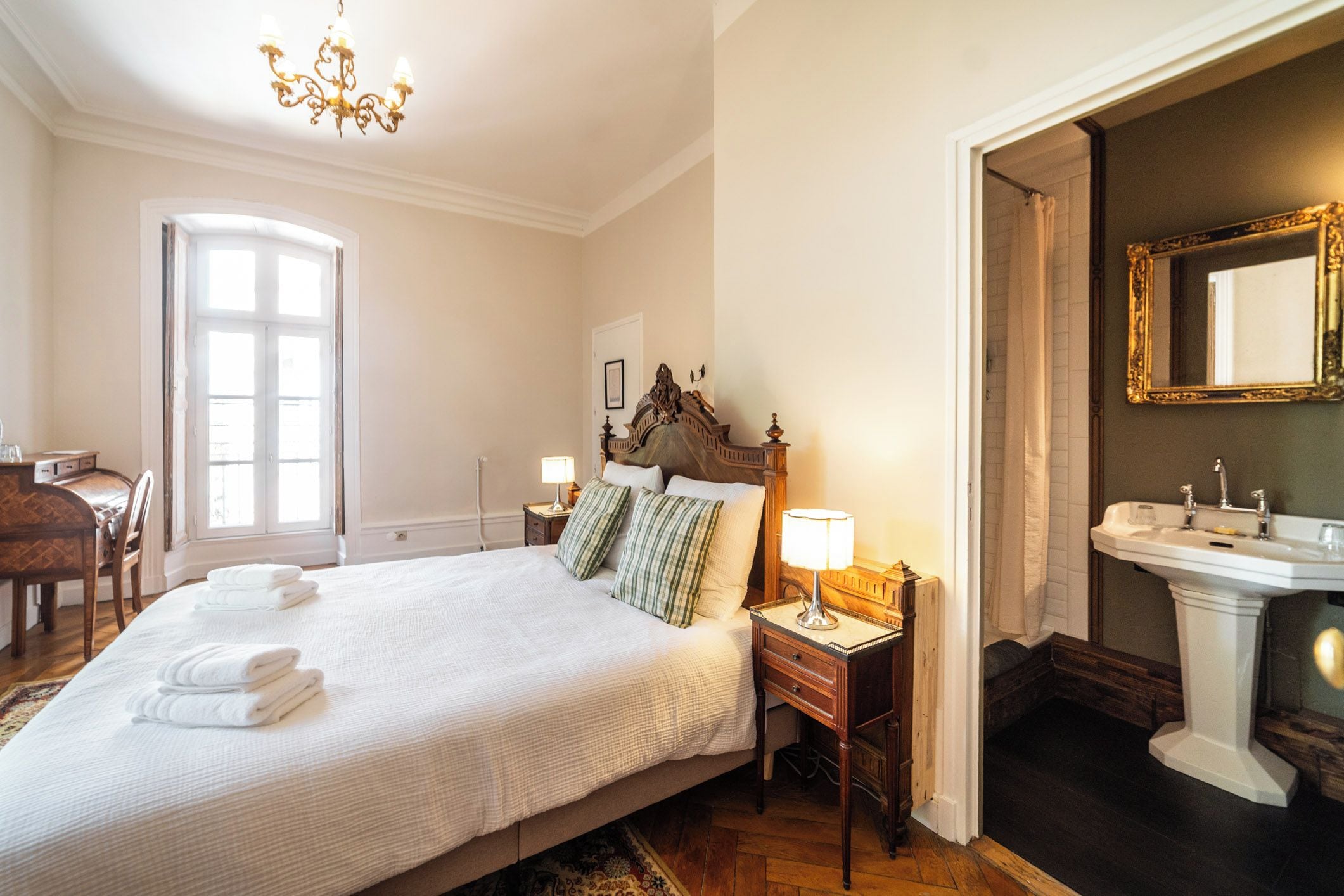 Habitación de hotel con una cama grande, lámparas de noche, una mesita de noche de madera y un baño con espejo y lavamanos.