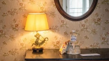 Un aparador de madera con un espejo encima, una lámpara sobre el aparador y un fondo de papel tapiz con motivos florales.