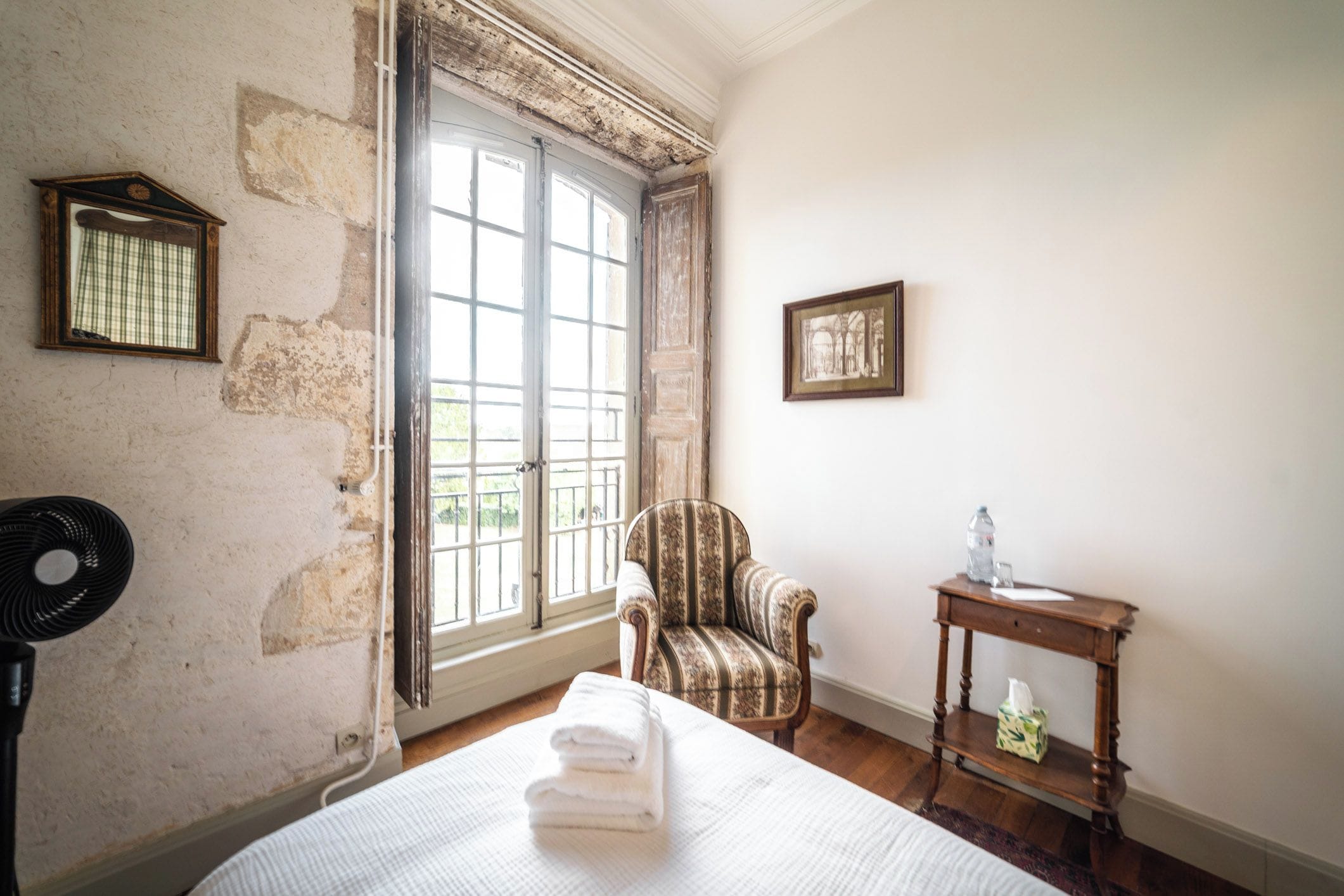 A room with a bed, a chair, a table, and a window with a view.