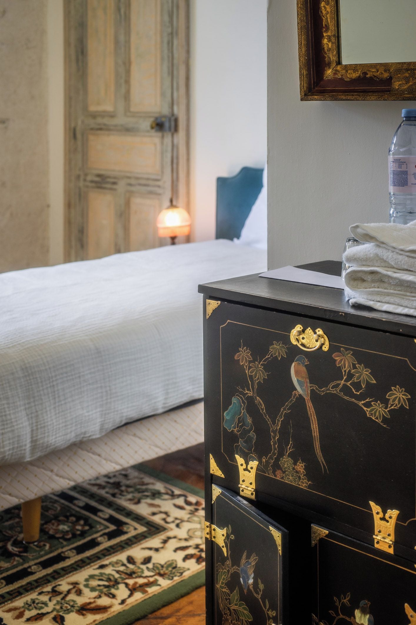 A hotel room with a bed, a dresser with decorative carvings, a mirror, and a lamp.