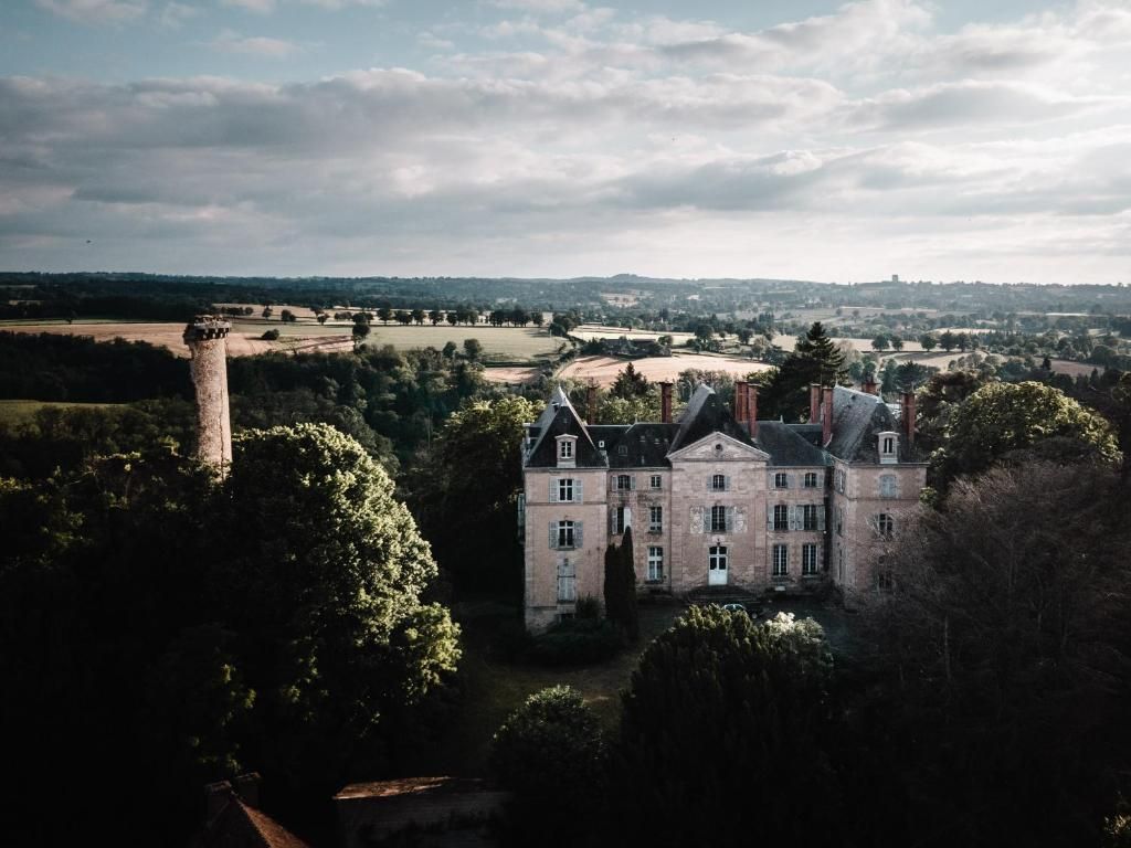 Un bâtiment historique doté d’une tour imposante, entouré d’une végétation luxuriante et d’un vaste domaine.