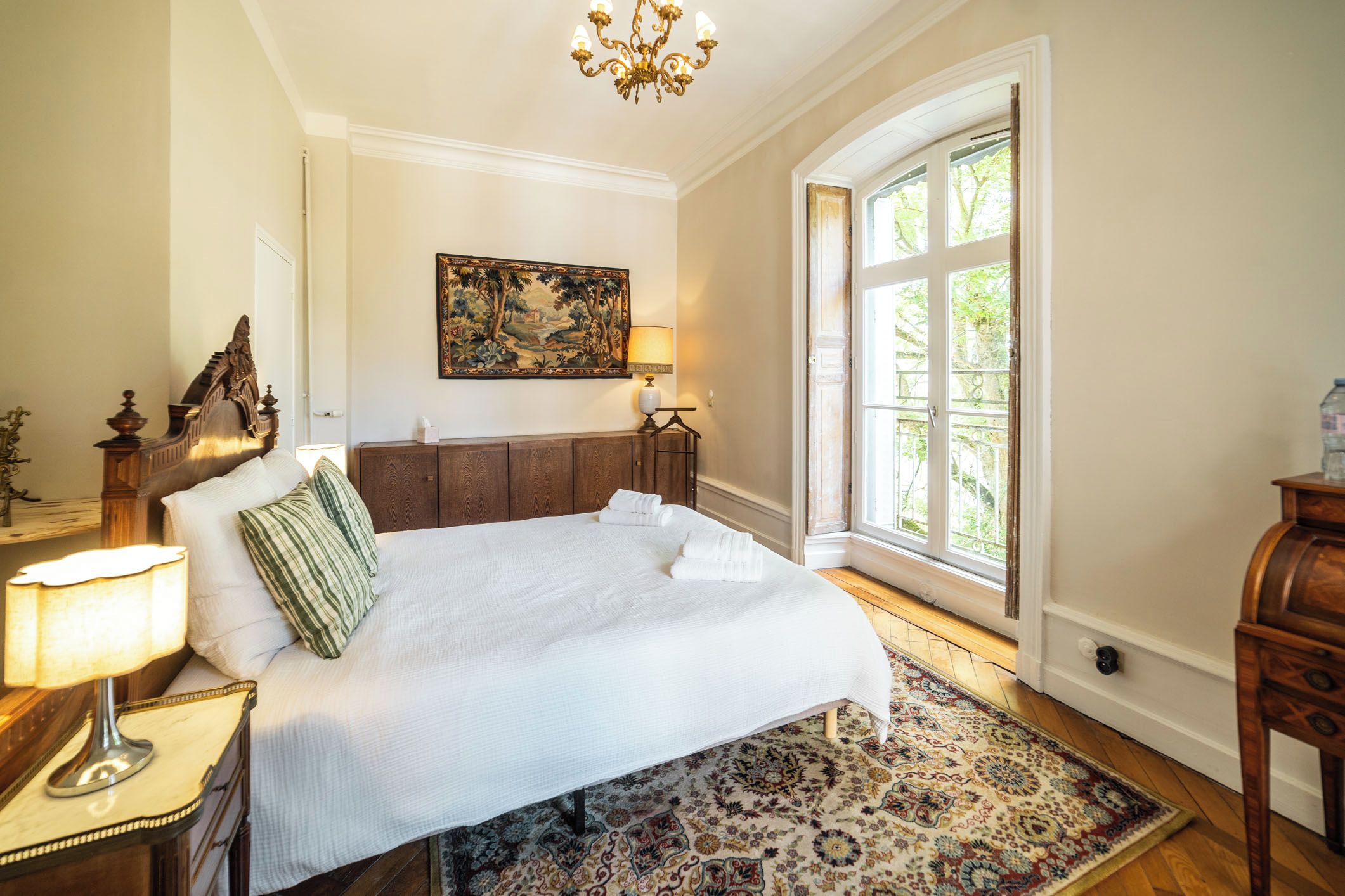 Une chambre bien éclairée, avec un grand lit, un tableau accroché au-dessus et une fenêtre laissant entrer la lumière naturelle.