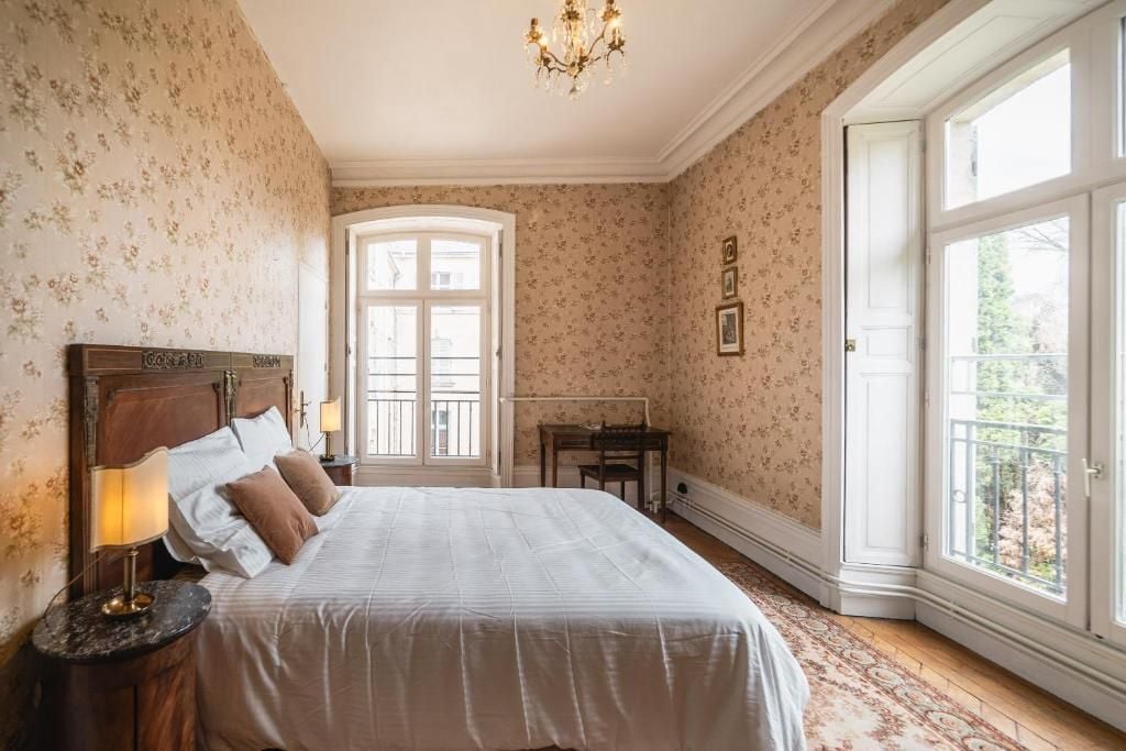 A bedroom with a large bed, a nightstand, a desk, and a window with a view.