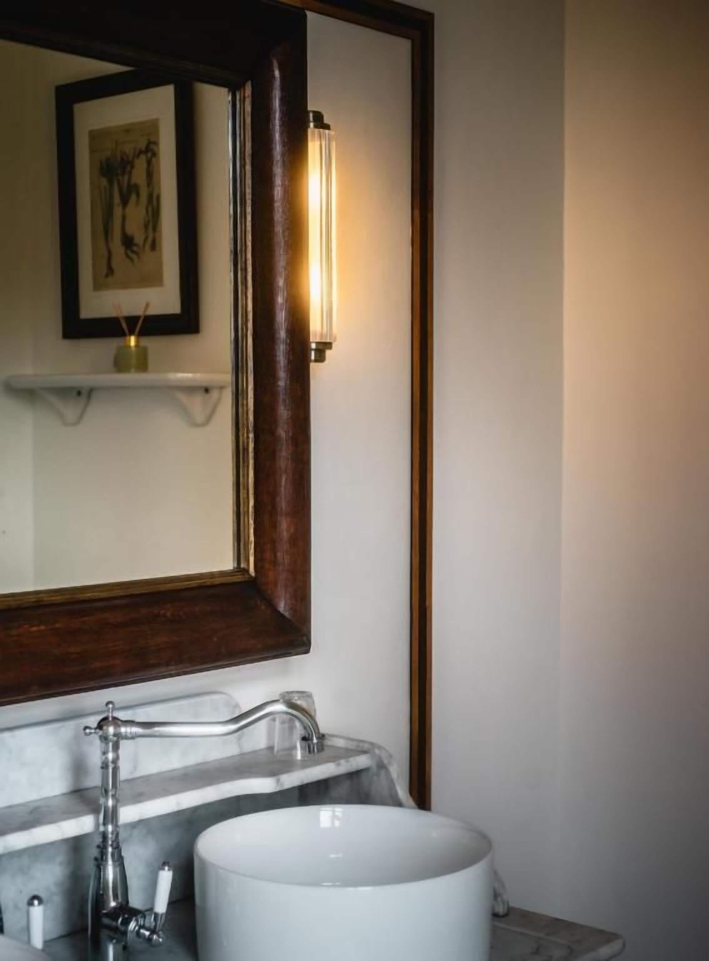 A bathroom with a marble sink, a framed mirror, and a wall-mounted light fixture.