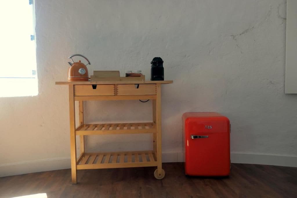 Ein Holztisch mit Schubladen und Regalen, ein roter Kühlschrank und ein Fenster mit Jalousien.