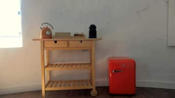 Ein Holztisch mit Schubladen und Regalen, ein roter Kühlschrank und ein Fenster mit Jalousien.
