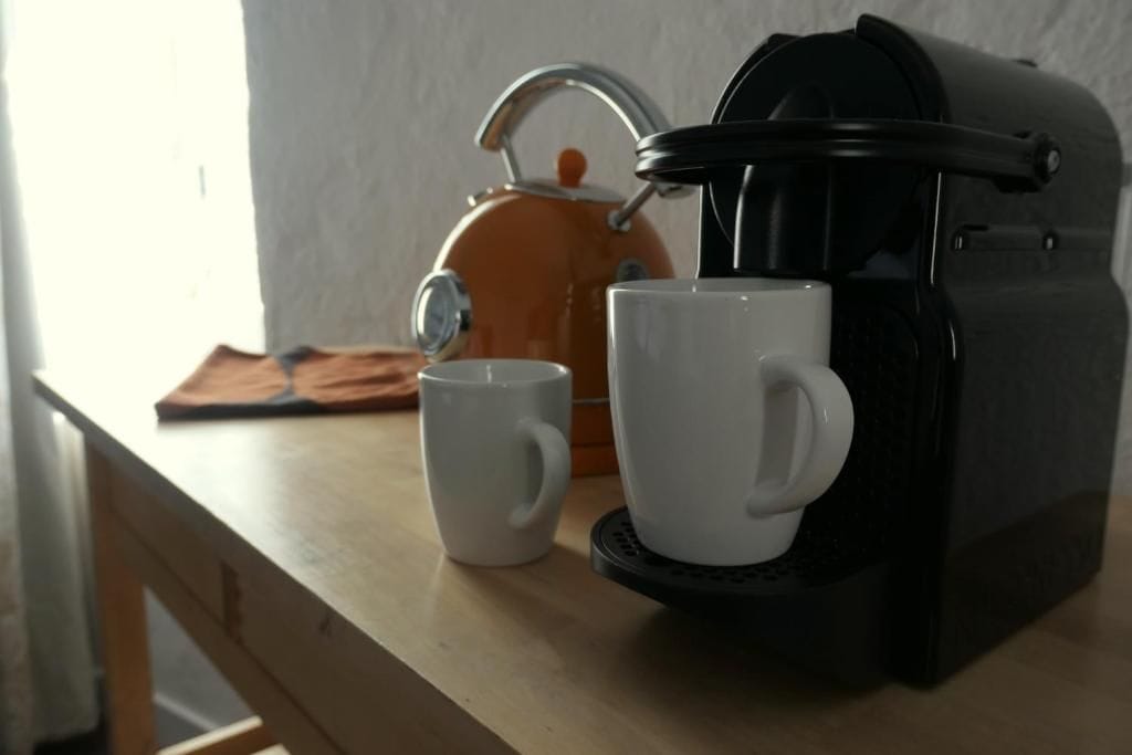 Una cafetera, dos tazas blancas y un hervidor sobre una mesa de madera.
