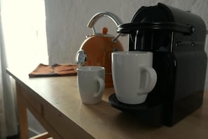 Una cafetera, dos tazas blancas y un hervidor sobre una mesa de madera.