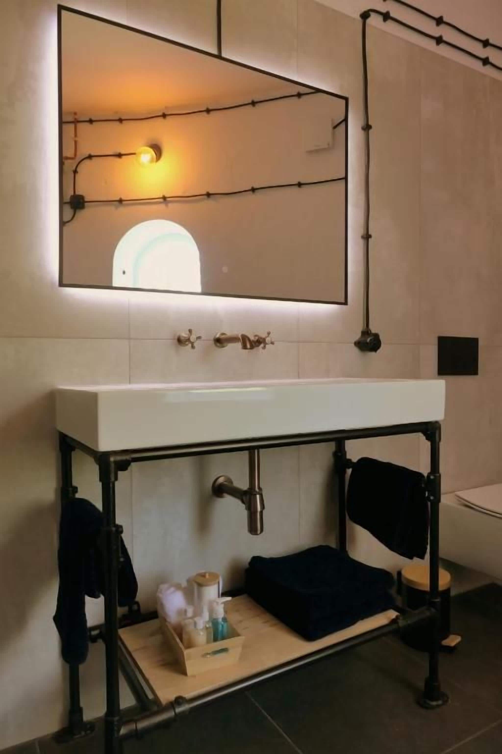 Un baño con lavamanos blanco, espejo y toallero.