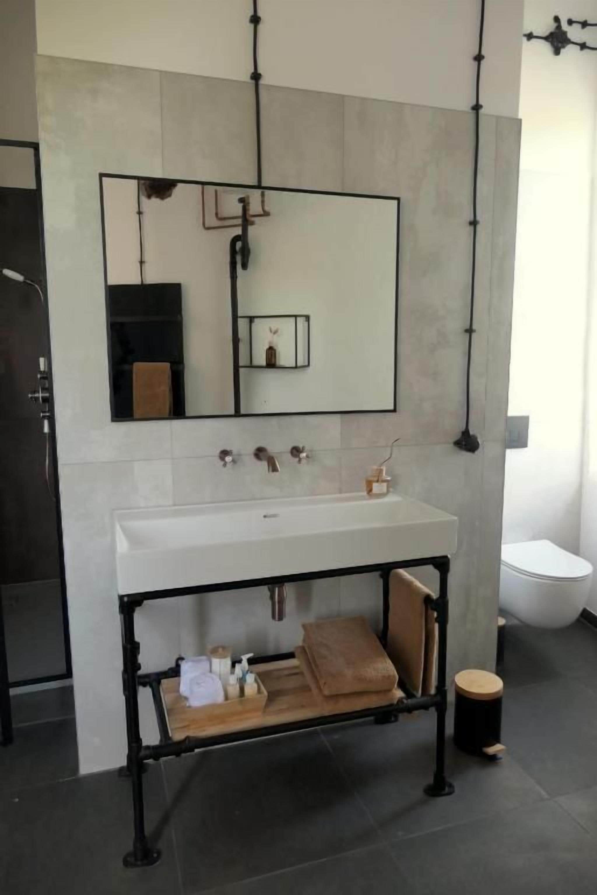 Un baño moderno con un lavamanos blanco, un espejo y un estante metálico negro.