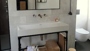 Un baño moderno con un lavamanos blanco, un espejo y un estante metálico negro.