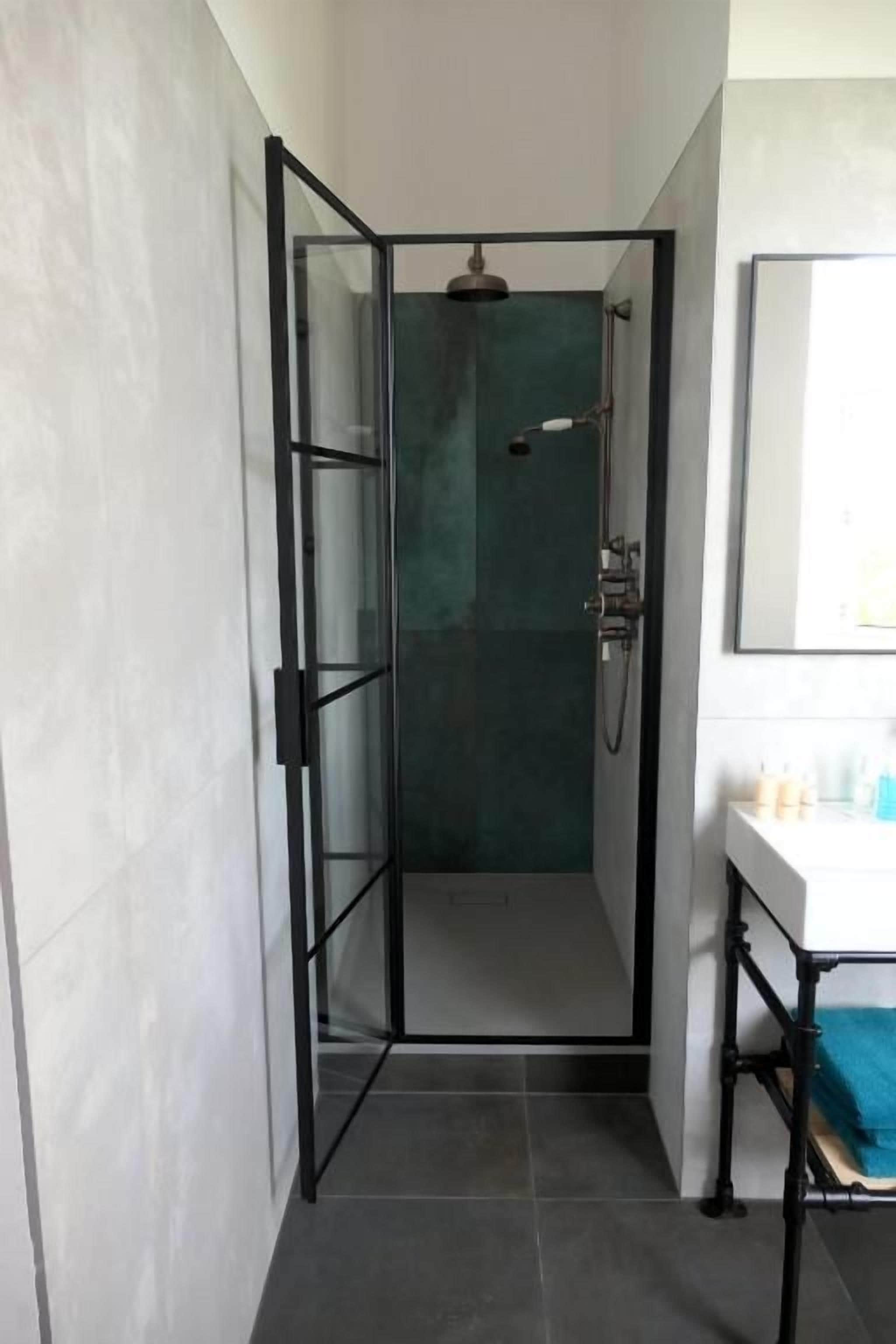 Ein modernes Badezimmer mit einer gläsernen Dusche, einem weißen Waschbecken und einem Spiegel darüber.