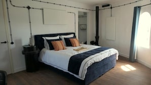 Un dormitorio con cama, mesitas de noche, un calentador de pared y una ventana con cortinas.