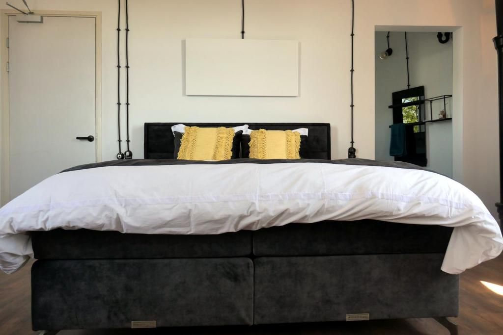 Una cama con cabecera negra y colcha blanca, dos almohadas y una lámpara fijada a la pared.