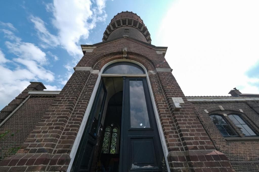Ein Backsteinhaus mit großem rundbogenförmigen Eingang und einem turmartigen Aufsatz.