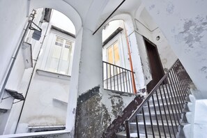 Eine Treppe mit Metallgeländern führt zu einer oberen Etage, umgeben von weißen Wänden mit abblätternder Farbe.