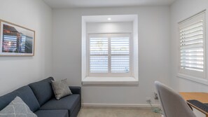 Ein Zimmer mit integriertem Fenster, einer Couch, einem Schreibtisch mit Tastatur und einem gerahmten Bild an der Wand.