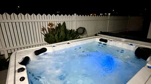 Un bain à remous avec jets, entouré d’une clôture blanche, et une plante en arrière-plan.