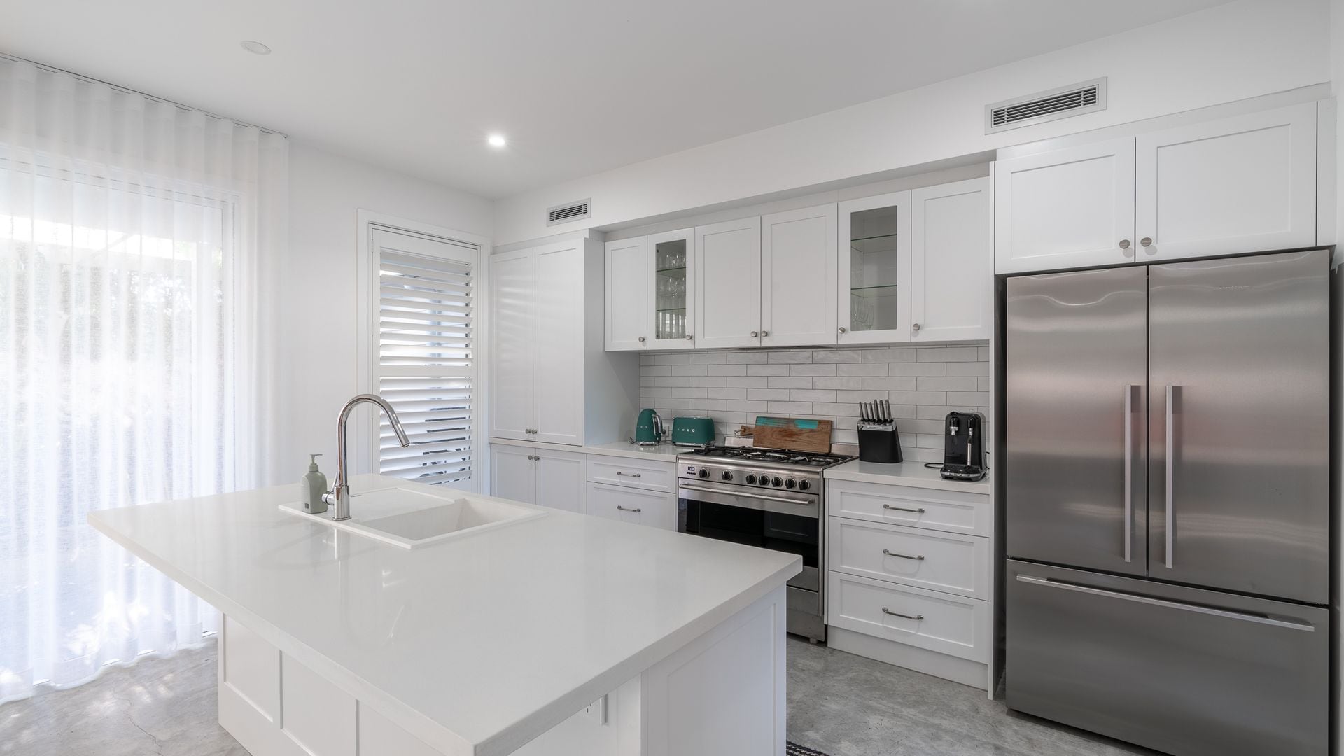 A modern kitchen with white cabinetry, a stainless steel refrigerator, and a central island with a sink.