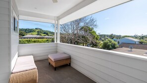Ein Balkon mit gepolsterten Sitzgelegenheiten, einem Korbsessel und Blick auf eine Wohngegend mit Häusern und Bäumen.