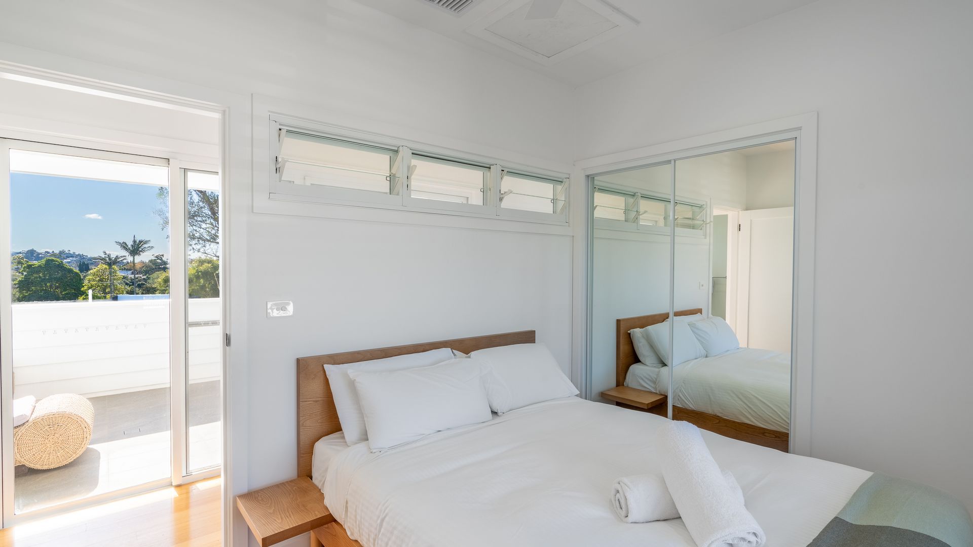 Quarto com cama, mesa de cabeceira, espelho e porta de vidro deslizante para uma varanda.