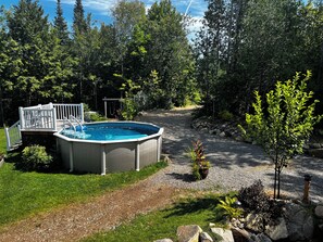 A swimming pool with a deck, surrounded by a gravel path and greenery. - 4-Bedroom Chalet with Spa and Pool in Rawdon (Rawdon)