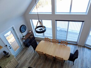 A dining area with a wooden table and chairs, a hanging light fixture, and large windows with a view of a wooden deck. - 4-Bedroom Chalet with Spa and Pool in Rawdon (Rawdon)