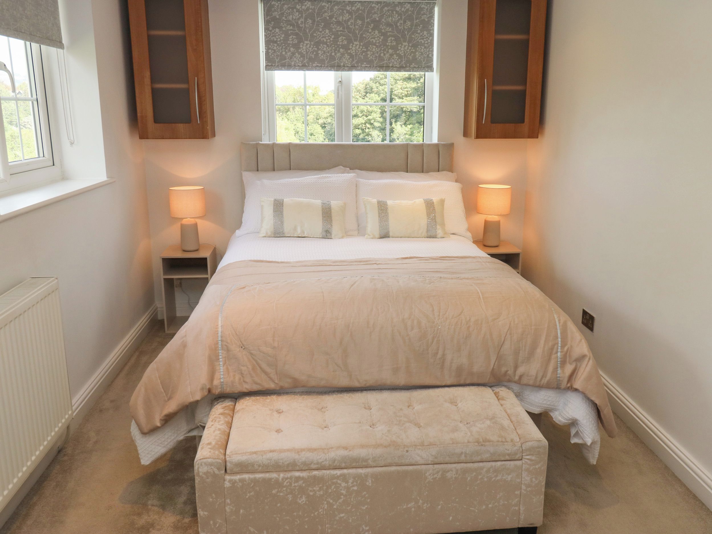 A bedroom with a bed, bedside lamps, a window with a view, and a radiator.